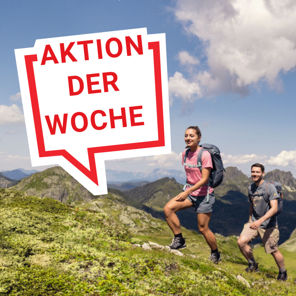 Zwei Personen wandern mit Rucksäcken auf einem üppig grünen Berghang. Sonderangebotstext: 'Aktion der Woche'.
