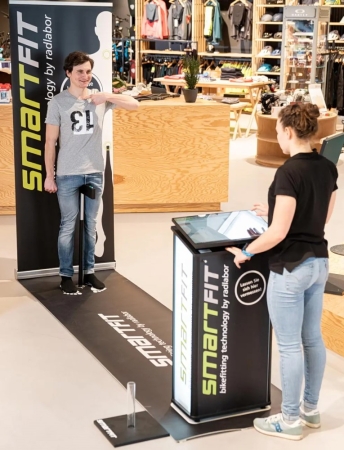 Ein Mann nutzt das SmartFIT Bikefitting-System für präzise Messungen, unterstützt von einer Frau in einem Einzelhandelsgeschäft.