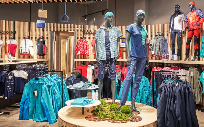 Modernes Interieur eines Sportgeschäfts mit Wänden voller Sneaker und zentralen Warenpräsentationen von Sportbekleidung und Accessoires.