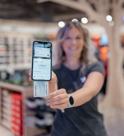 Woman in a retail store with a smartphone displaying a digital balance and a customer card.