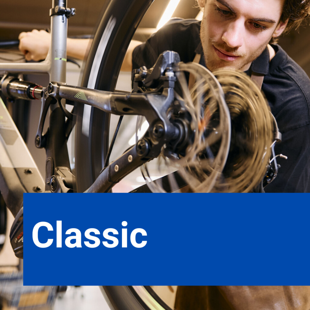 Ein junger Fahrradmechaniker arbeitet in einer Werkstatt an dem Hinterrad und der Scheibenbremse eines Fahrrads.