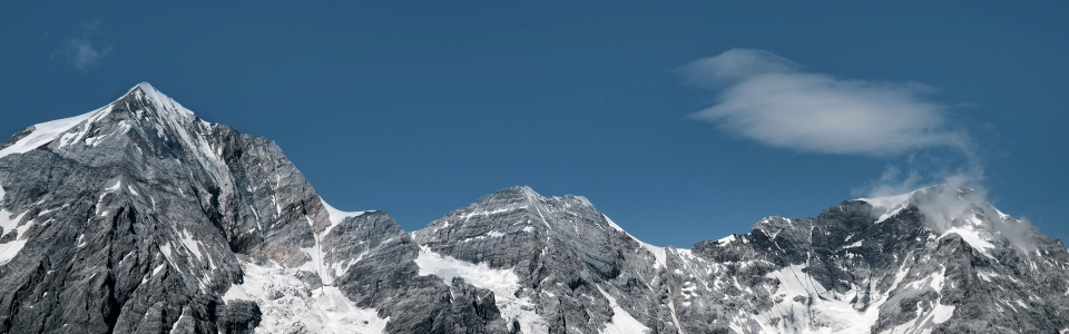 Panoramablick auf zerklüftete, schneebedeckte Berggipfel unter einem klaren blauen Himmel mit einer zarten Wolke.