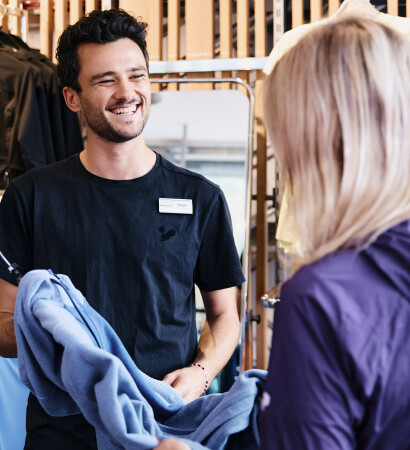 A smiling sales associate helps a customer and shows her blue clothing in a clothing store.