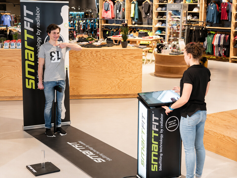 Ein Kunde nutzt das smartfit digitale Fußmesssystem in einem Einzelhandelsschuhgeschäft, unterstützt von einem Mitarbeiter.