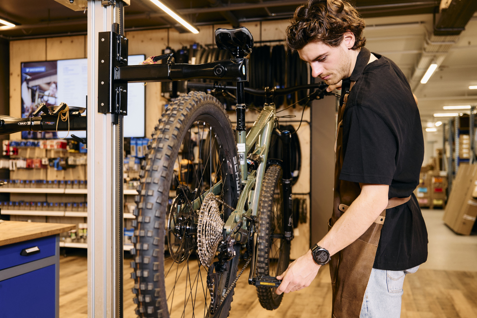 Ein Fahrradmechaniker wartet ein Mountainbike auf einem Montageständer in einem professionellen Fahrradgeschäft.