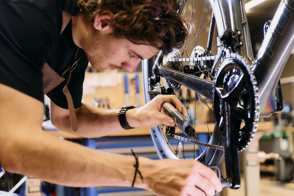 Ein Fahrradmechaniker stellt die Schaltung und Kette eines Rennrads mit einem Werkzeug in einer professionellen Werkstatt ein.
