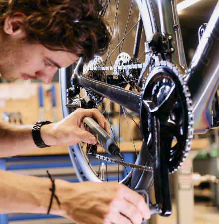 Ein männlicher Fahrradmechaniker führt in einer professionellen Werkstatt Wartungsarbeiten durch und stellt den Antrieb an einem Rennrad ein.