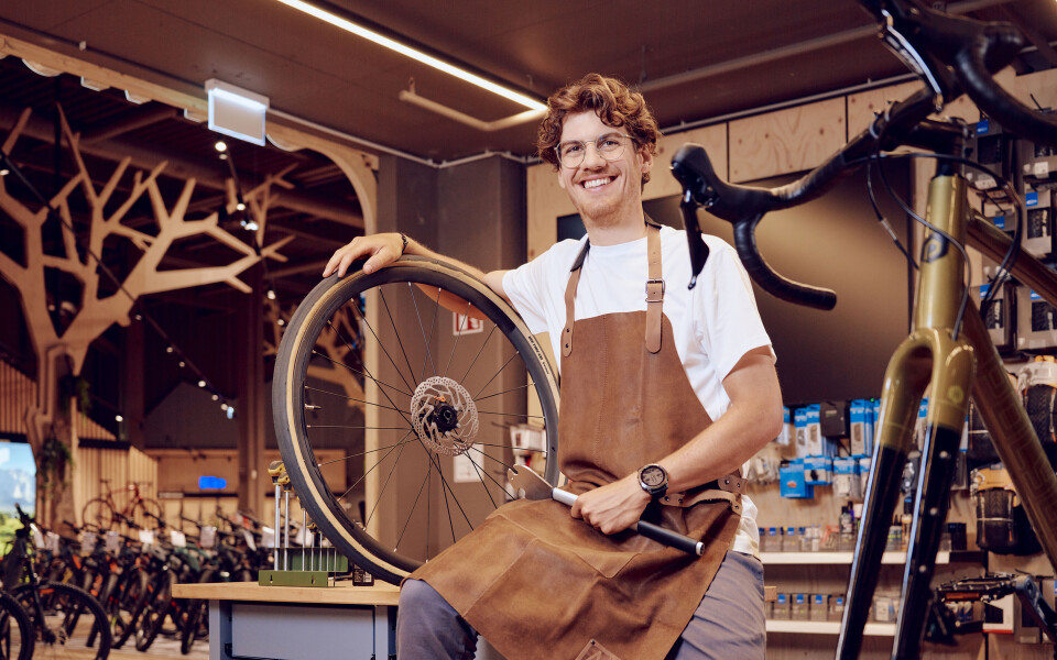 Ein lächelnder Fahrradmechaniker hält ein Fahrradrad in einer Gmundner Fahrradwerkstatt.
