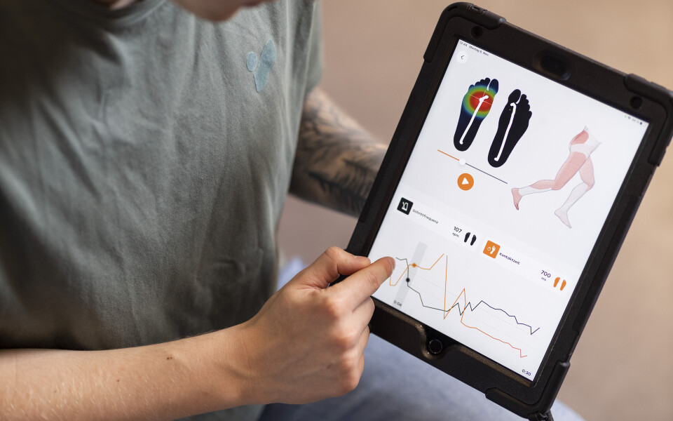 Ein Spezialist zeigt auf ein Tablet, das Daten zur Fußdruckkartierung und biomechanischen Ganganalyse darstellt.