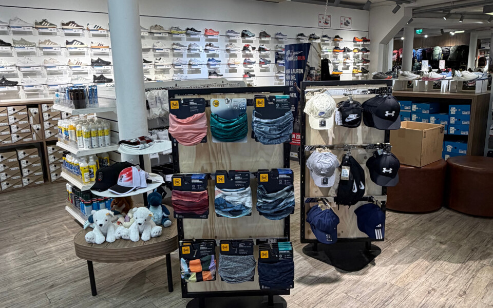 Modernes Interieur eines Sportgeschäfts mit Wänden voller Sneaker und zentralen Warenpräsentationen von Sportbekleidung und Accessoires.