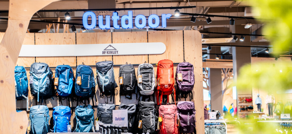 Auslage eines Outdoor-Geschäfts mit Wanderrucksäcken, Sportbekleidung und einem auffälligen „Outdoor“-Schild.
