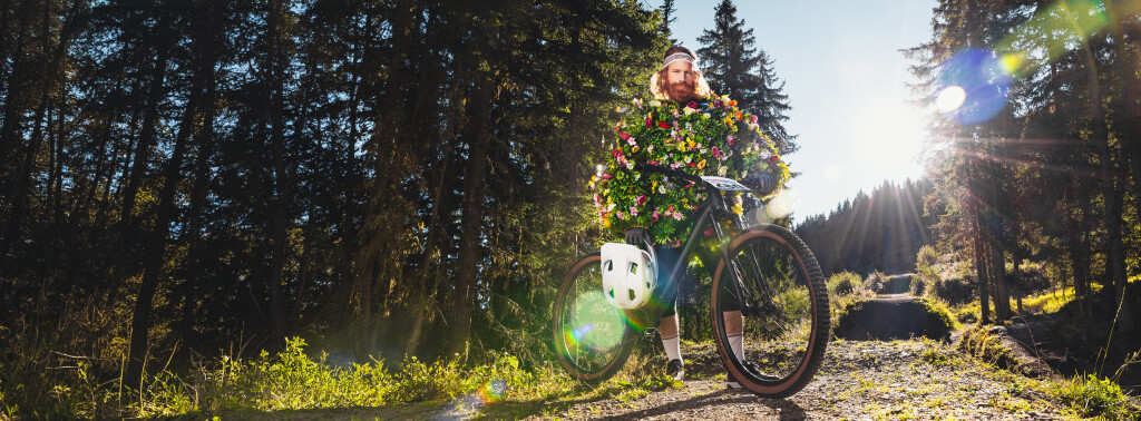 Ein Radfahrer fährt auf einem Schotterweg durch einen sonnendurchfluteten Wald, wobei helles Sonnenlicht durch die Bäume filtert.