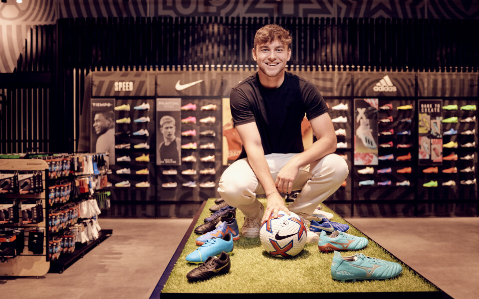 Lächelnder Mann hockt in einem Sportschuhgeschäft und hält einen bunten Fußballschuh