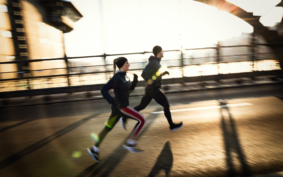 Two athletes run during the golden hour on a city bridge, showcasing outdoor fitness and a healthy lifestyle.
