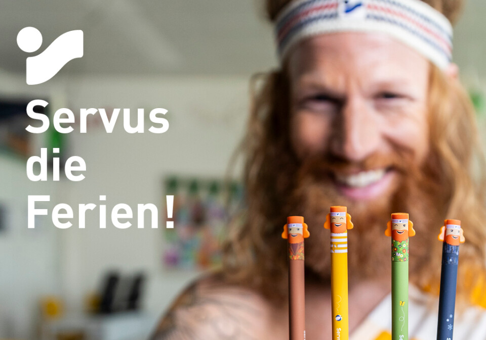 Intersport ad: Smiling man in a headband and toga holds colorful "Servus die Ferien!" pencils, promoting a free stationery set.