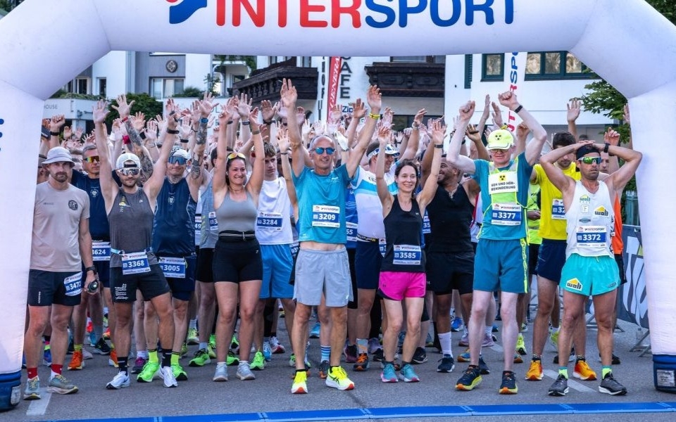 Begeisterte Athleten mit erhobenen Armen unter einem Intersport-Bogen bei einer Laufveranstaltung.